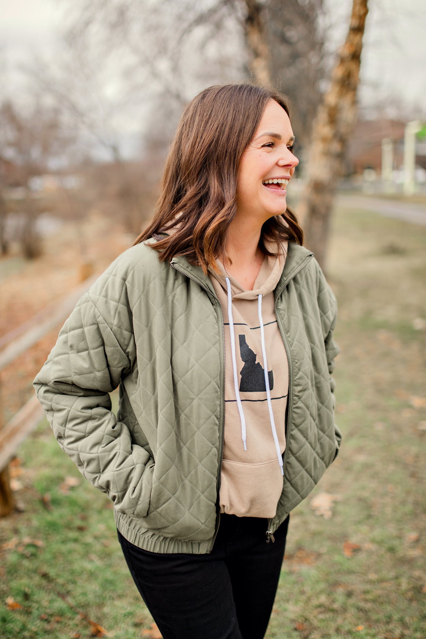 An Idaho mama wearing a tan Idaho hoodie. The hoodie is nicknamed the coziest hoodie in Idaho because it really is that coziest. This tan hoodie has a simple Idaho design on it.