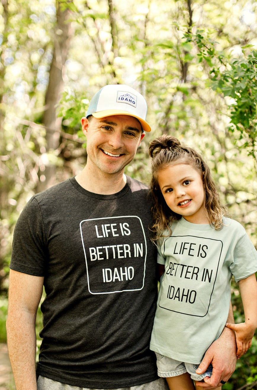 A dad and his daughter proudly wearing their Idaho T Shirts standing outside in Idaho. The T Shirt says Life is Better in Idaho. Idaho is the best place to live!