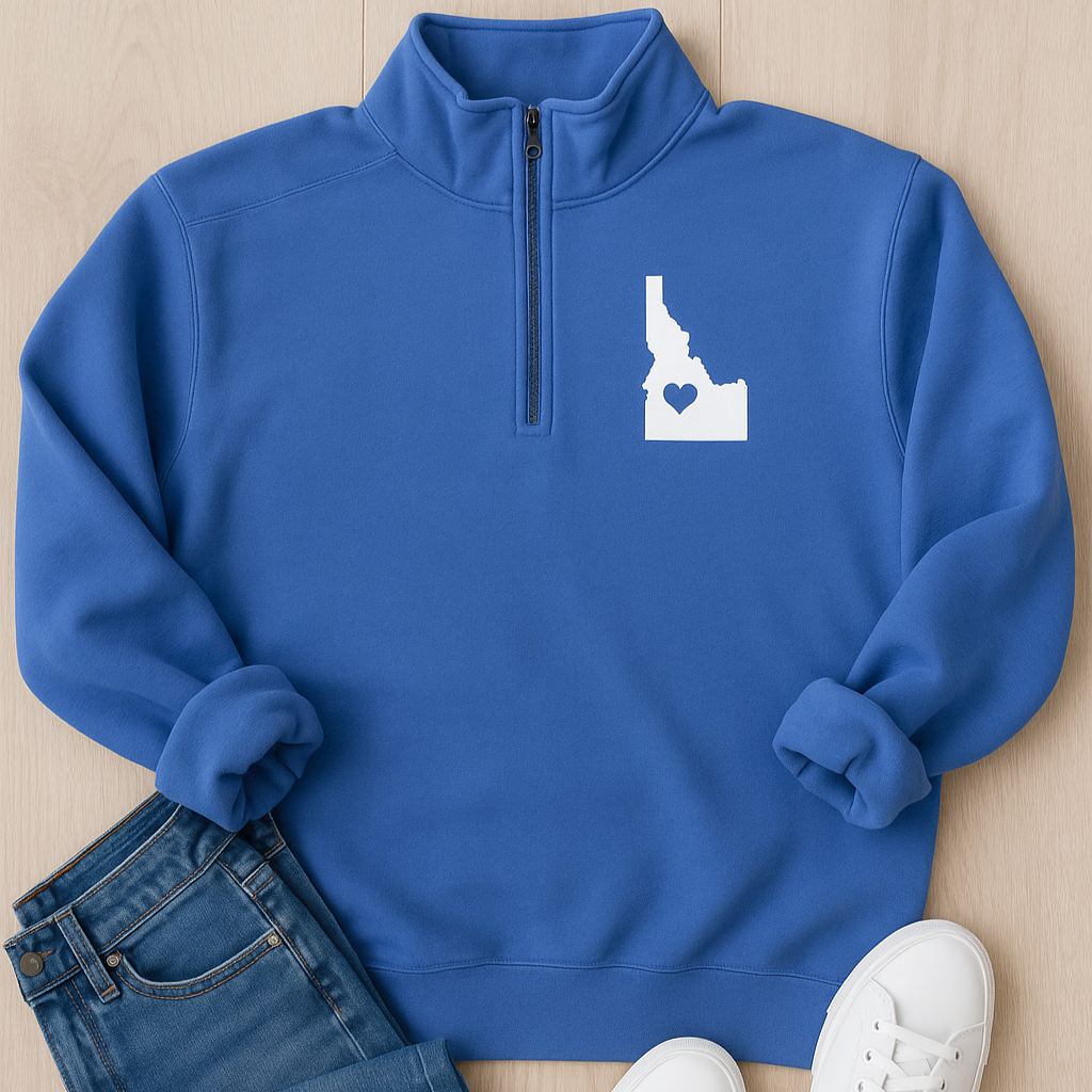 Blue pullover with Idaho design, blue jeans, and white sneakers on a wooden surface