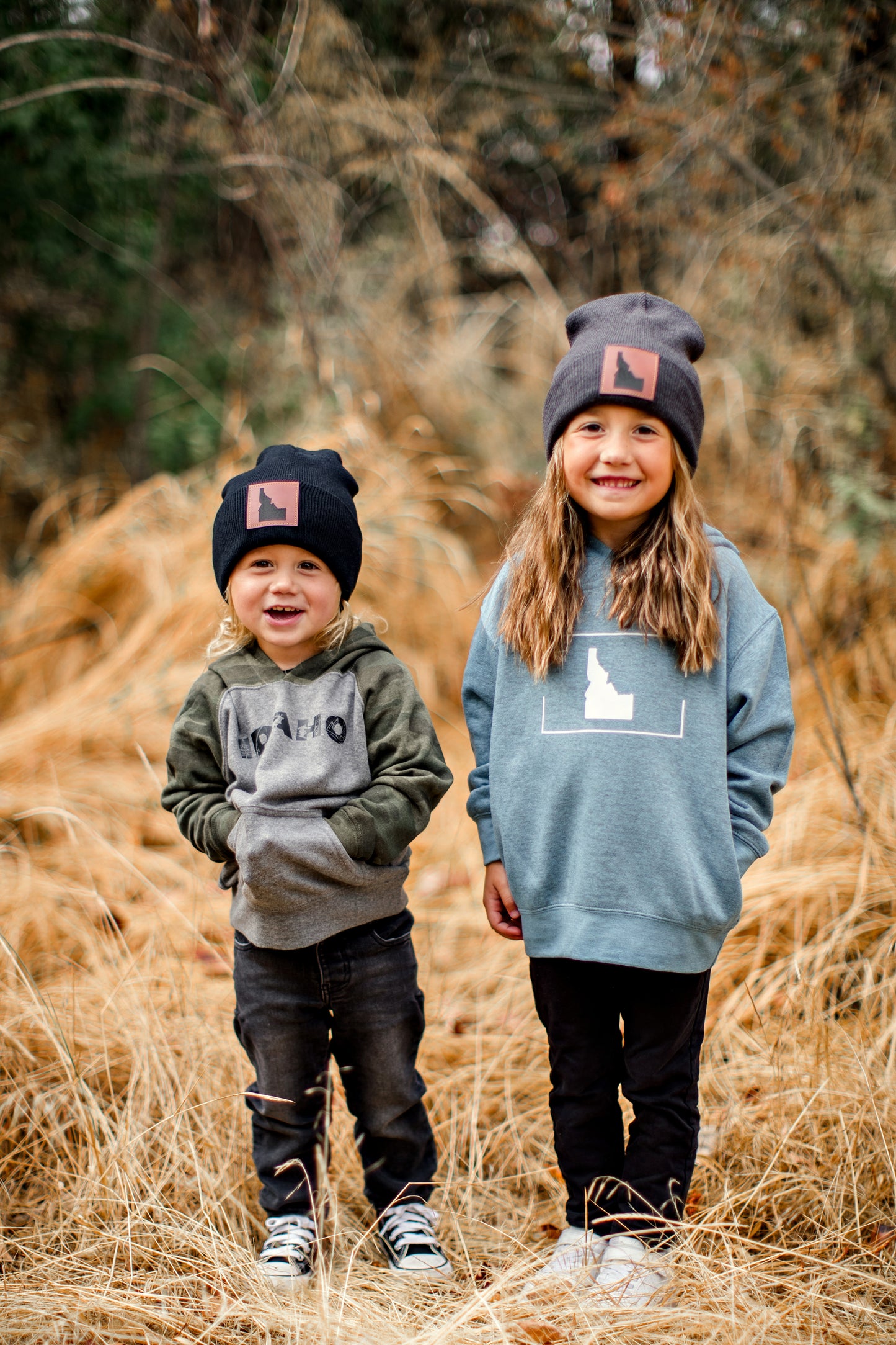 The brother and sister are wearing Idaho sweatshirts. The sweatshirts are blue and one is camo. The simple Idaho designs on the front are designed by TatorJo, an Idaho clothing company