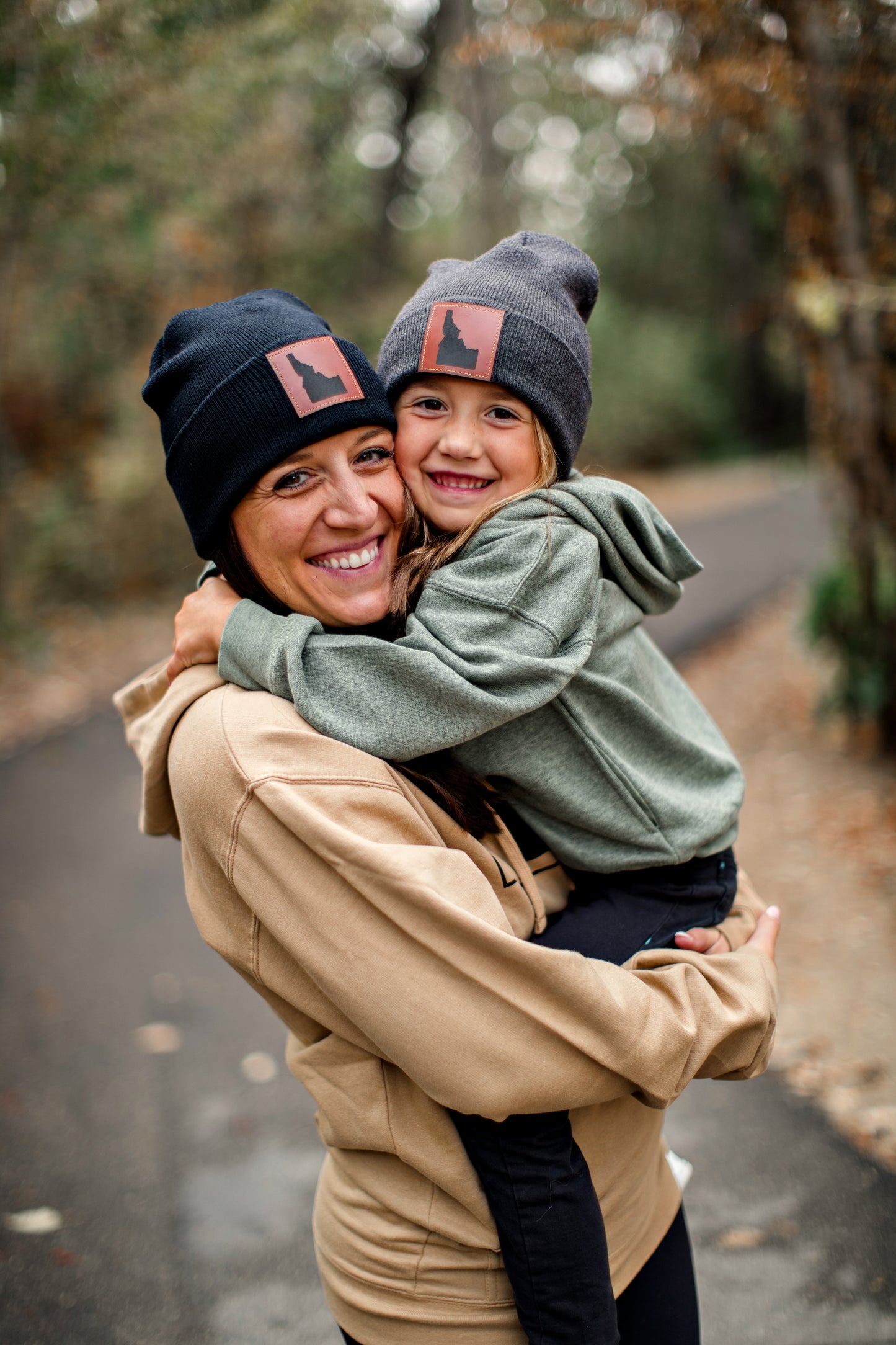 A mom and daughter standing outside in Idaho wearing their Idaho beanies. The mom is wearing a black Idaho beanie and the daughter is wearing a gray Idaho beanie. These Idaho beanies are made by TatorJo, an Idaho clothing company. This Idaho hat will keep you warm all winter.
