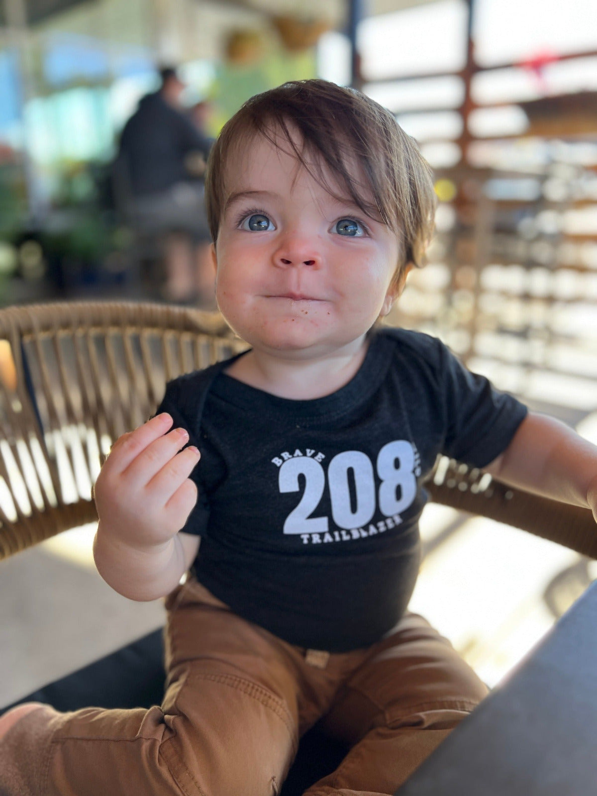 A little boy wearing an Idaho onesie that says 208 Trailblazer. He is eating a piece of something and looking so cute!