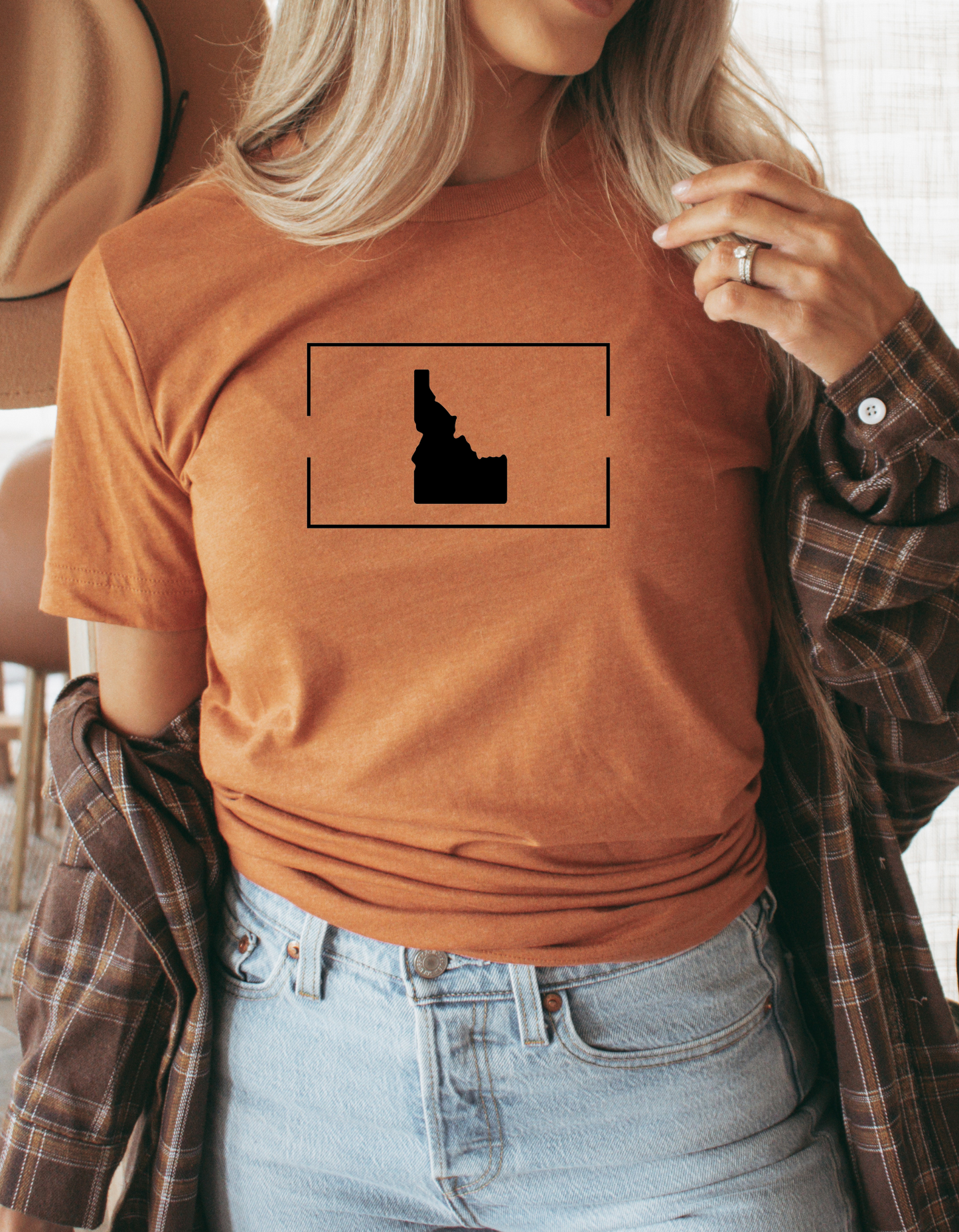 A woman wearing an orange Idaho-themed t-shirt with a minimalist black Idaho state outline. Ideal for showcasing Idaho-inspired apparel for women or Idaho men, highlighting local pride.