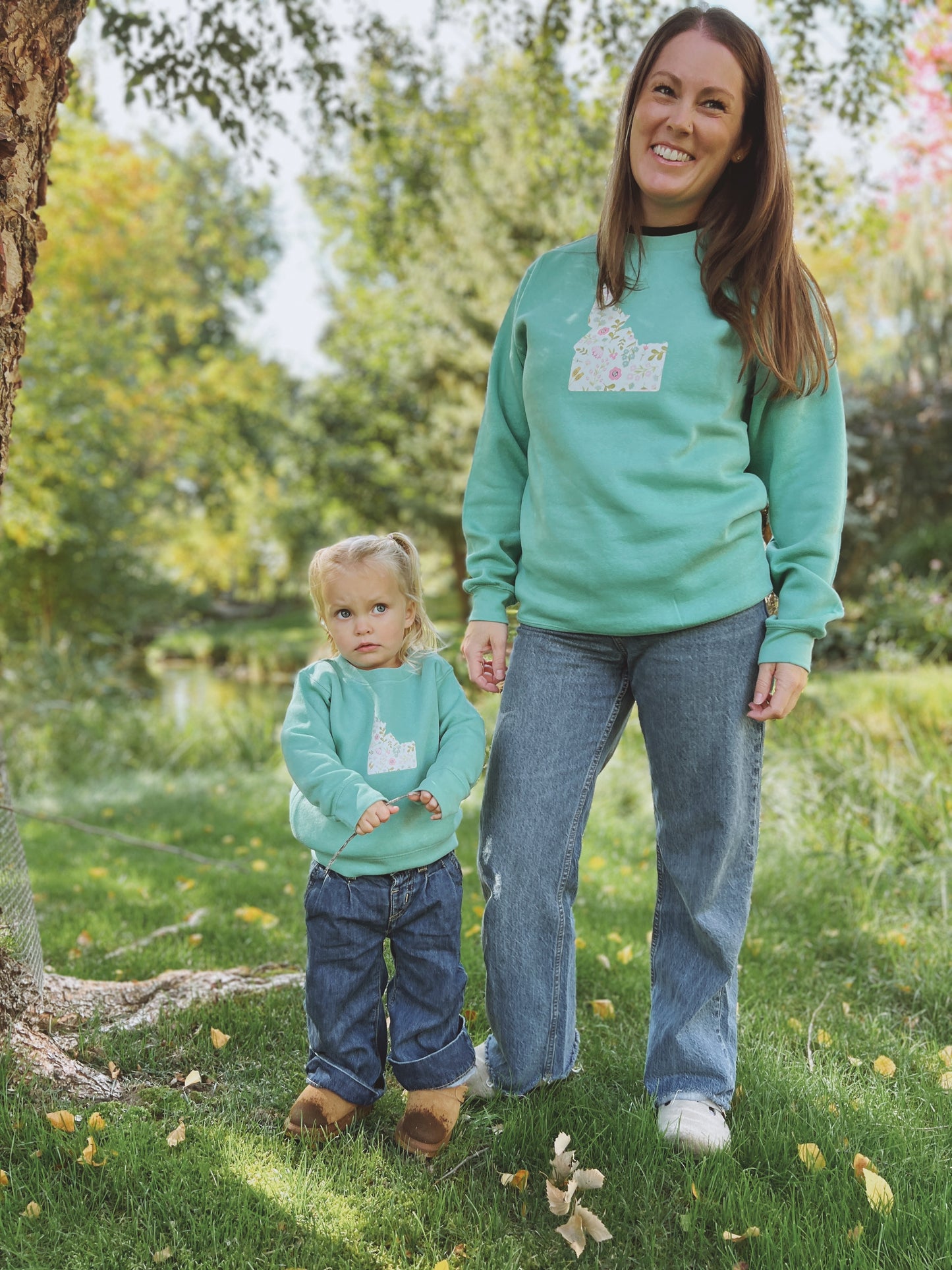 Woman and child wearing matching green sweaters with an Idaho design on it. Idaho sweaters with an Idaho clothing company
