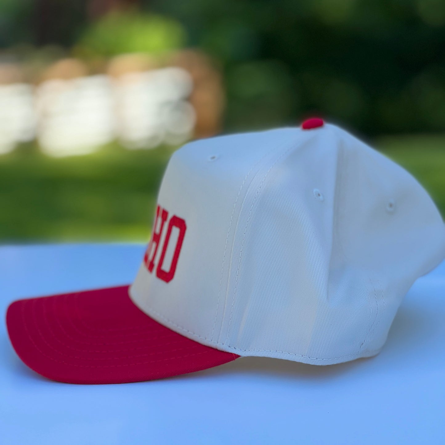 White cap with red brim and 'Idaho' on a white surface with blurred green background