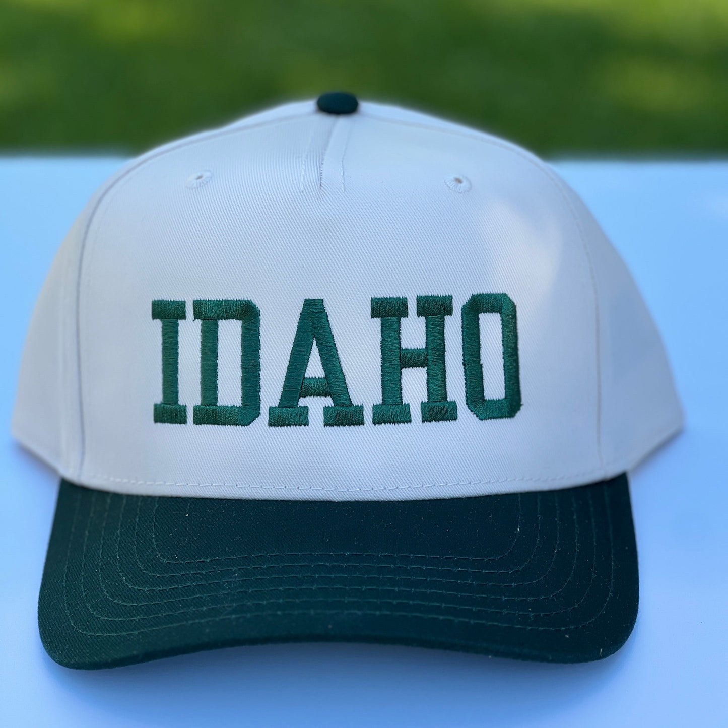 White Idaho hat cap with 'Idaho' in green on a white surface with blurred green background