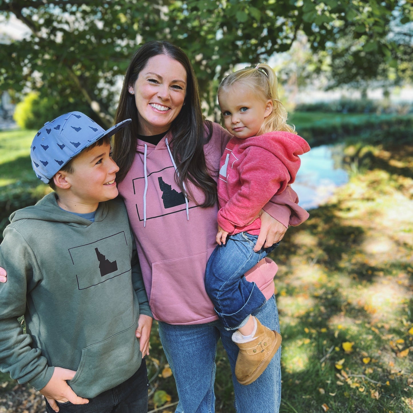 A mom and two Idaho kids standing outside in Idaho wearing matching hoodies. The hoodies have Idaho on them.