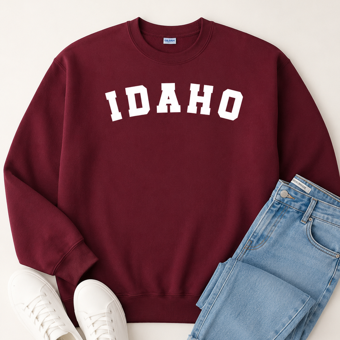 Maroon sweatshirt with 'IDAHO' text, white sneakers, and blue jeans on a light background