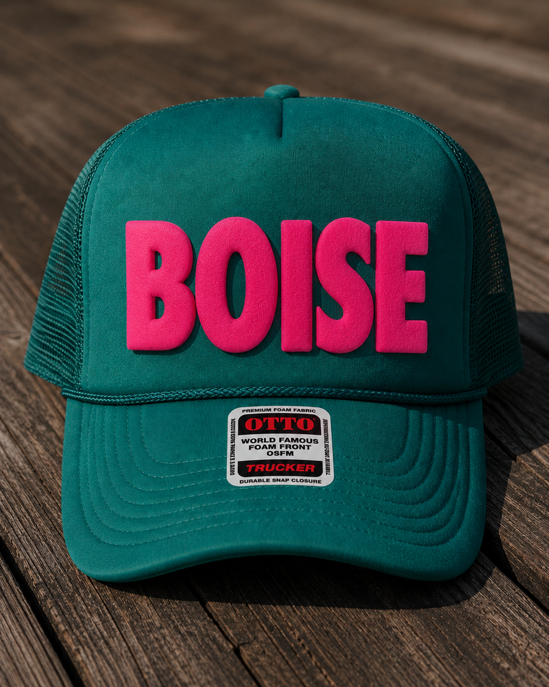 Teal cap with pink 'BOISE' text on a wooden surface