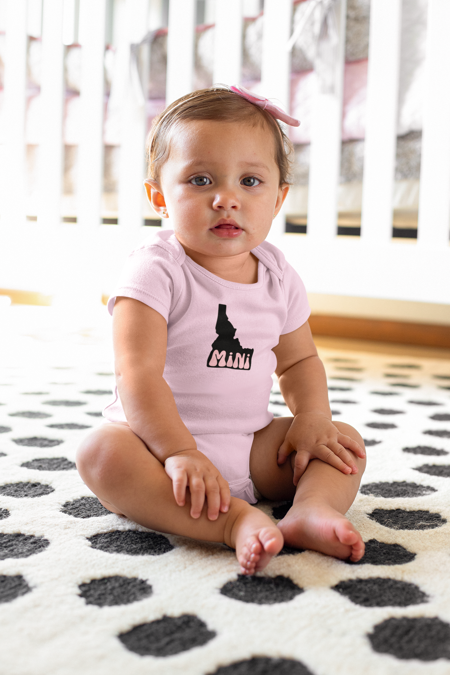 The Idaho baby is wearing an adorable pink onesie that says Idaho on it. THe Idaho onesie is the design of an Idaho with mini in it