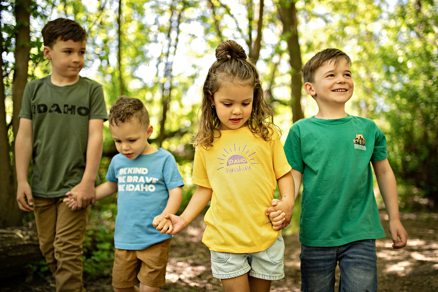 Four kids playing outside in Idaho, the kids are wearing Idaho shirts. They are holding hands and smiling for the photo.