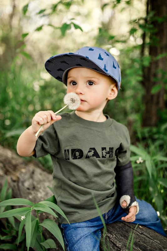 This Idaho T Shirt has adventure graphics designed inside the Idaho. It comes in a soft military green and can be worn by toddlers up to adult. This Idaho T Shirt showcases the things we love about Idaho. It has a pine tree inside the I, fishing inside the D, elk inside the A, Sking and paddle boarding inside the H and camping inside the O. All the outdoor adventures that Idaho has to offer.