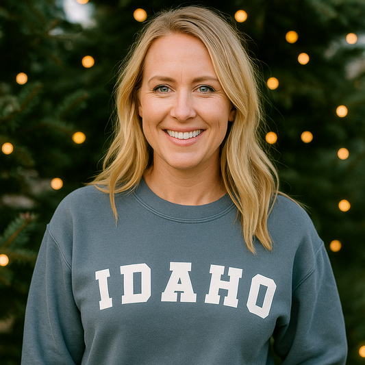 Woman wearing a blue sweatshirt with 'Idaho' printed on it, standing in front of a decorated Christmas tree.
