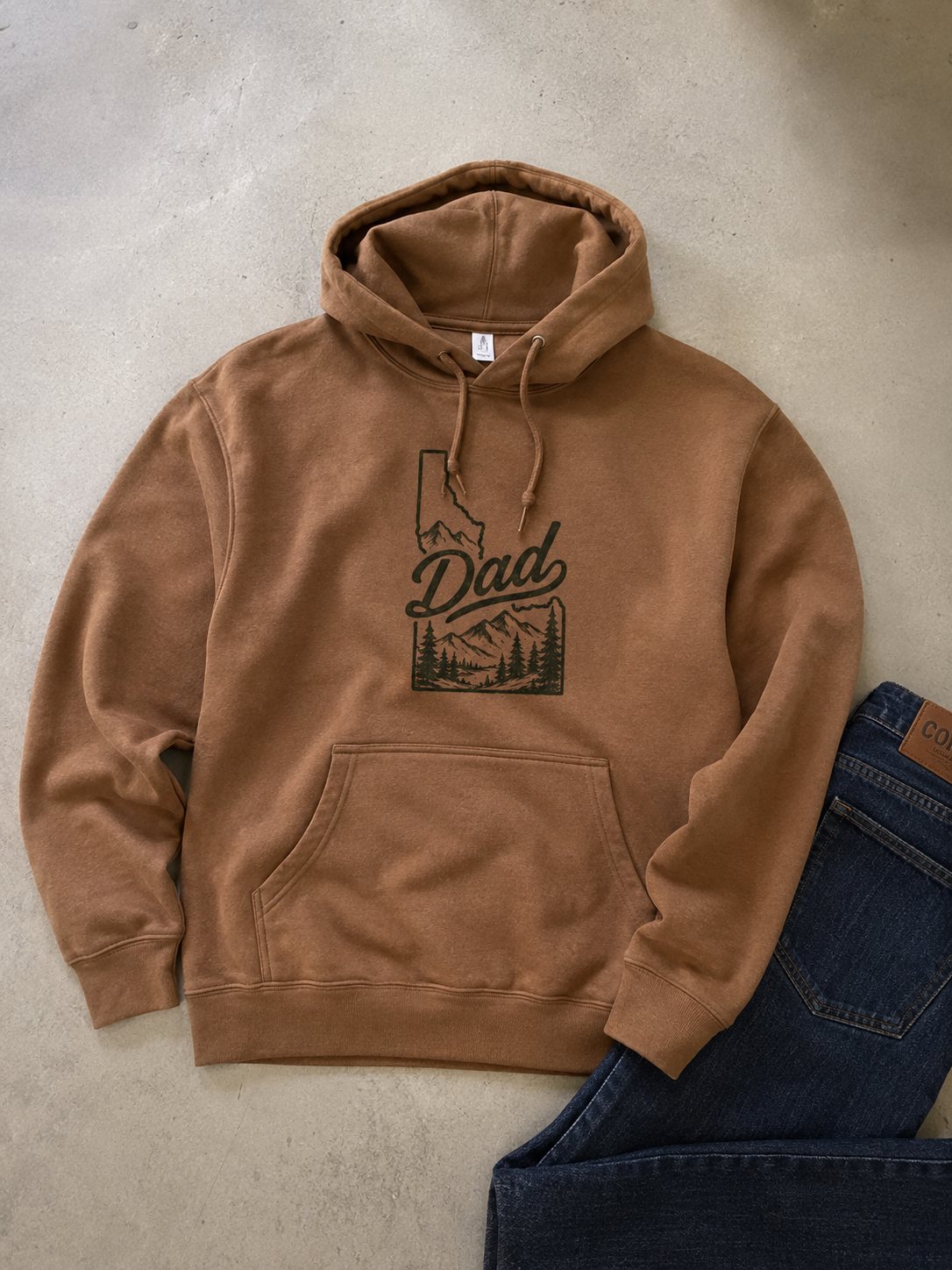 Brown hoodie with 'Dad' and mountain design on a concrete surface