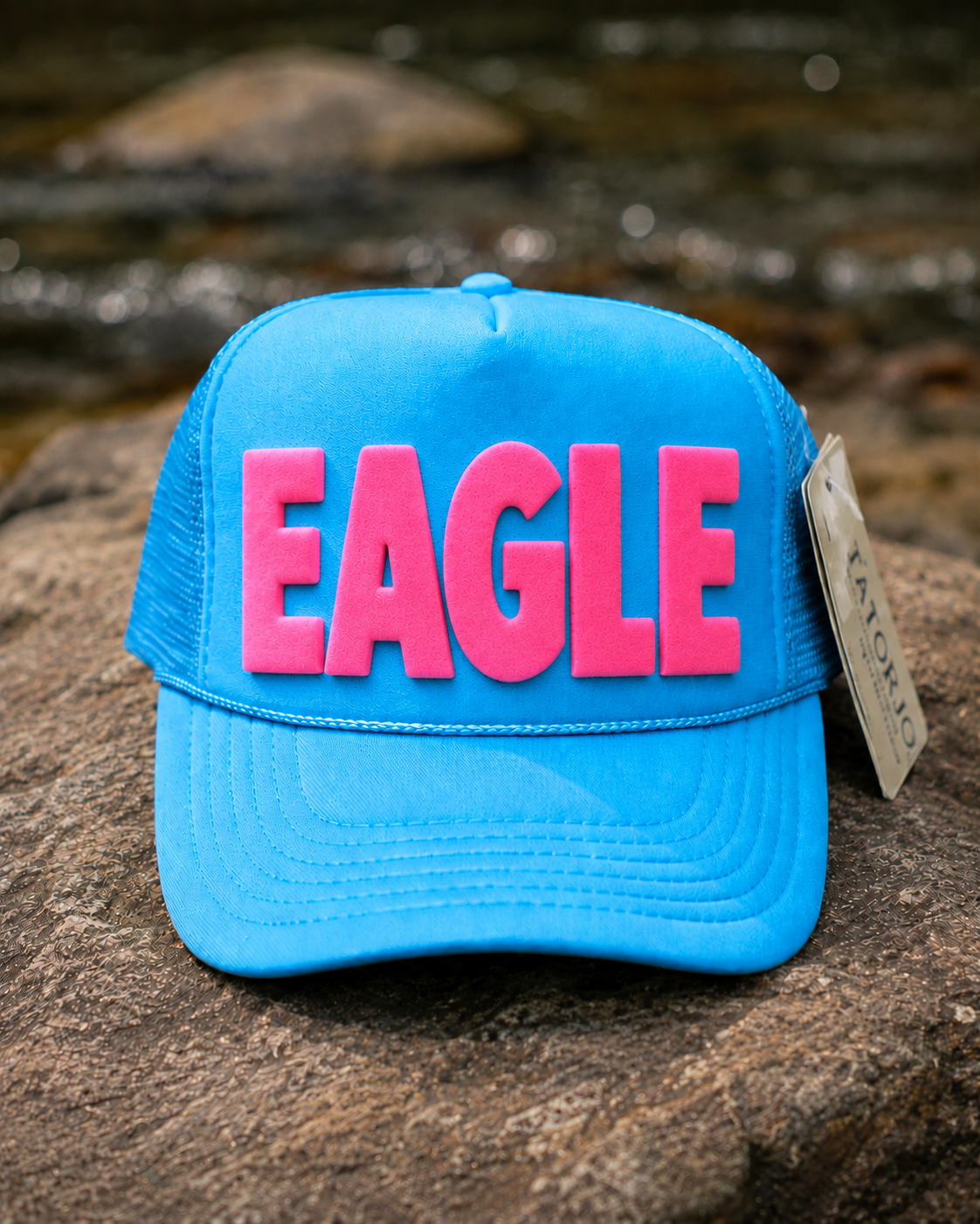 Blue cap with pink 'EAGLE' text on a rock with water background