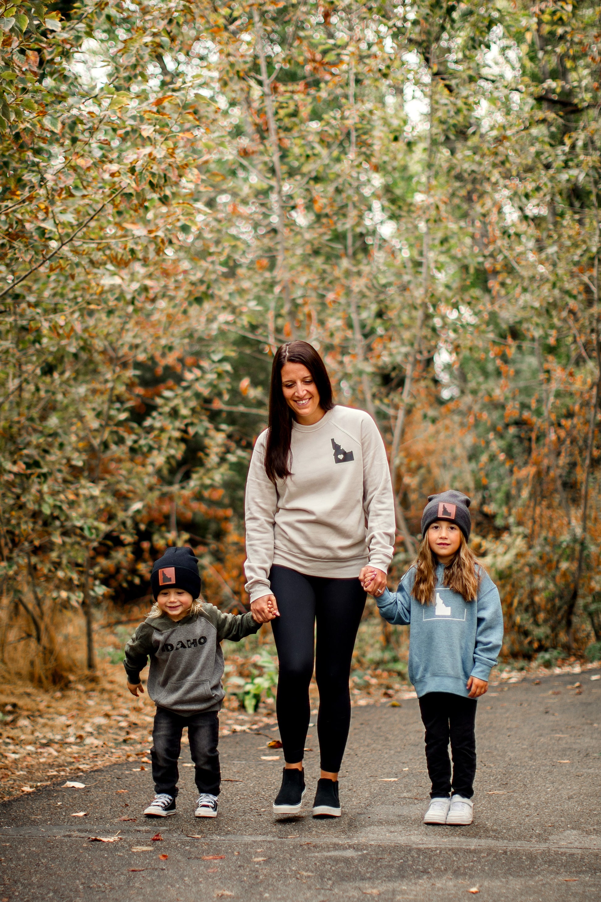 Mom and two kids walking in Idaho. The mom is wearing a natural colored crewneck with a small Idaho on it. The kids are wearing Idaho sweatshirts that are made by TatorJO. an Idaho apparel company