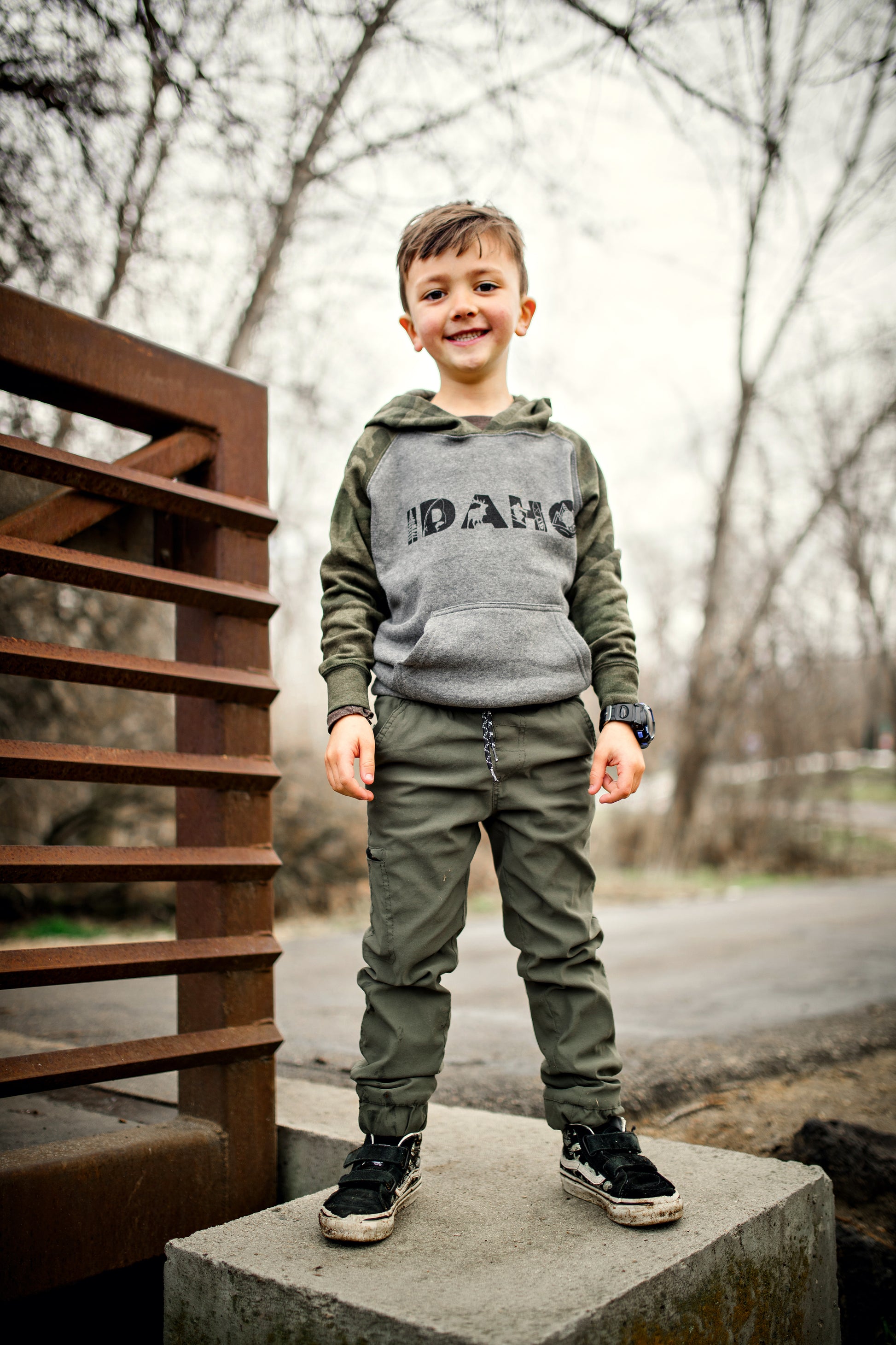 A young boy standing outside in an Idaho hoodie. The hoodie has Idaho on it and has camo on the sleeves.
