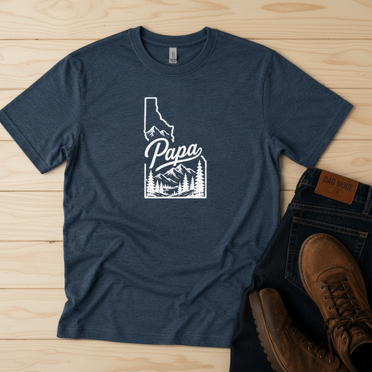 Navy blue t-shirt with 'Papa' and Idaho outline design on a wooden surface with brown boots.