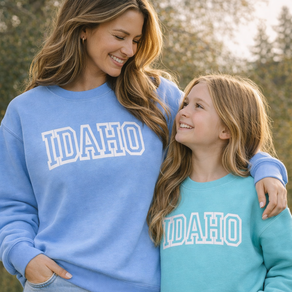 A mom and daughter standing outside wearing Puff Print Idaho Sweaters. The sweaters read Idaho on them. 