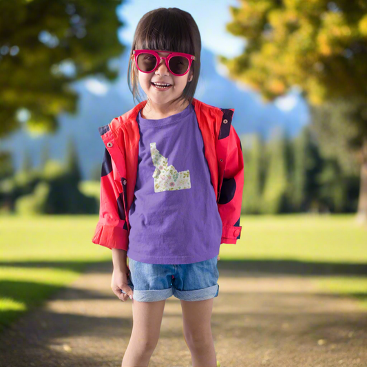 Idaho girl wearing a a purple t shirt that has an Idaho design on it. THe idaho design is floral, super cute! Little girl is stylish in her Idaho swag