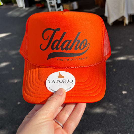 Orange cap with 'Idaho' branding held by a hand against a dark background