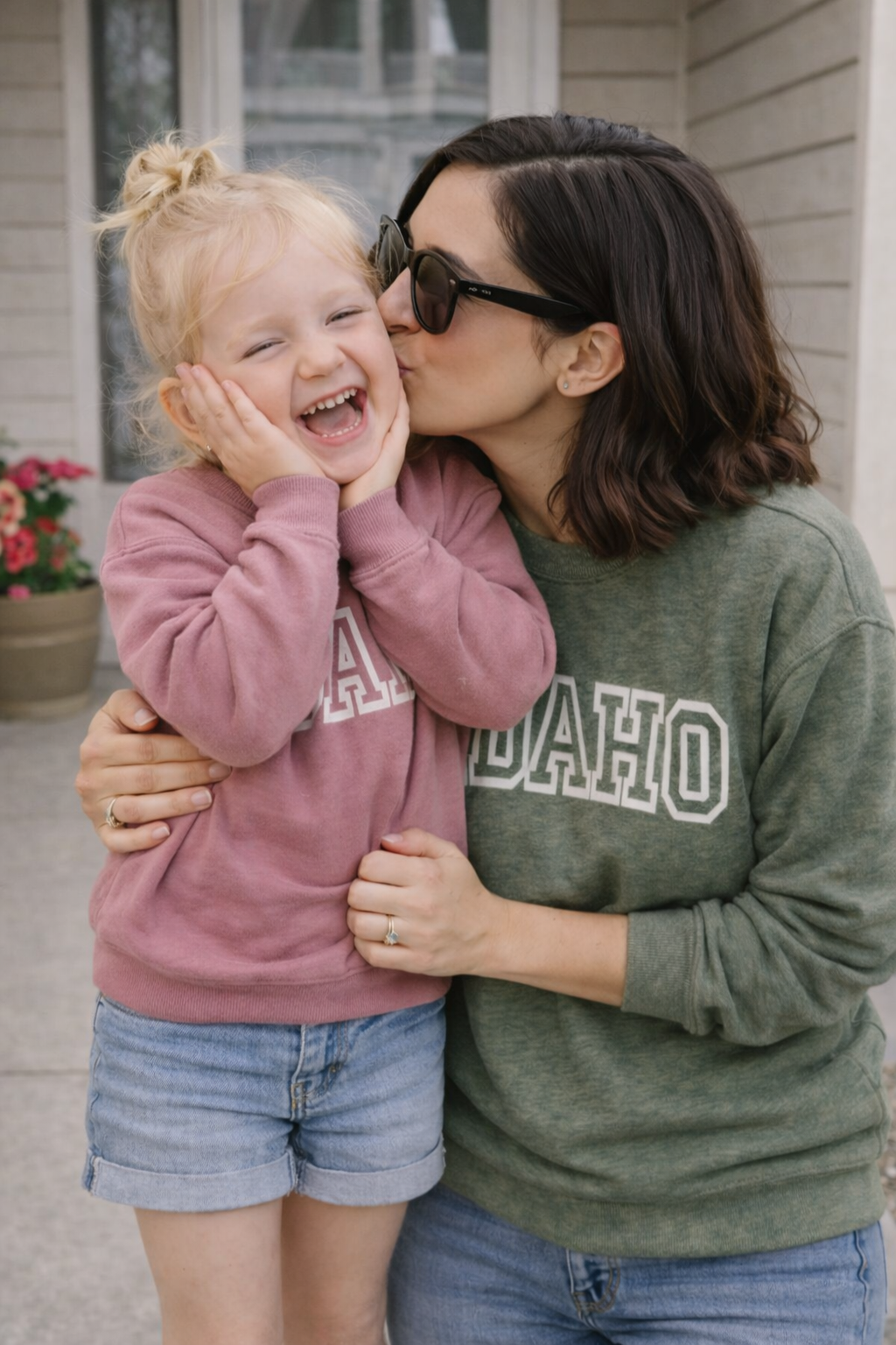 Woman kissing a child on the cheek outdoors, both wearing sweatshirts with 'Idaho' text.