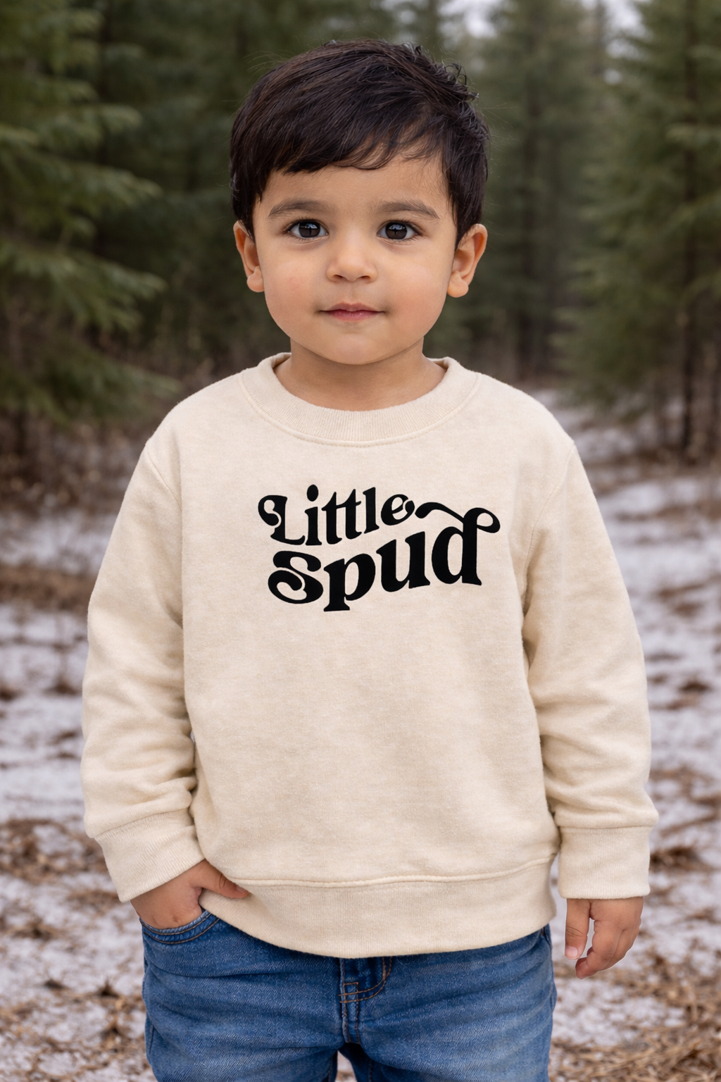 Child wearing a 'Little Spud' sweatshirt in a forest setting. Little Spud is designed by TatorJo an Idaho Apparel company