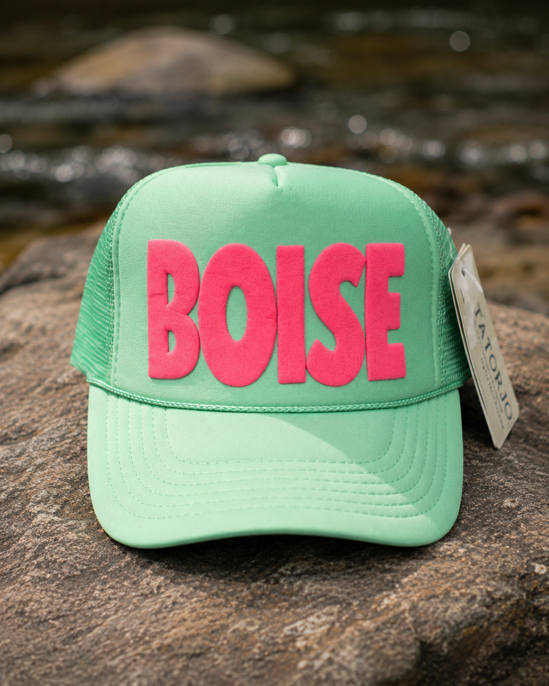 Green cap with 'BOISE' in pink on a rock surface